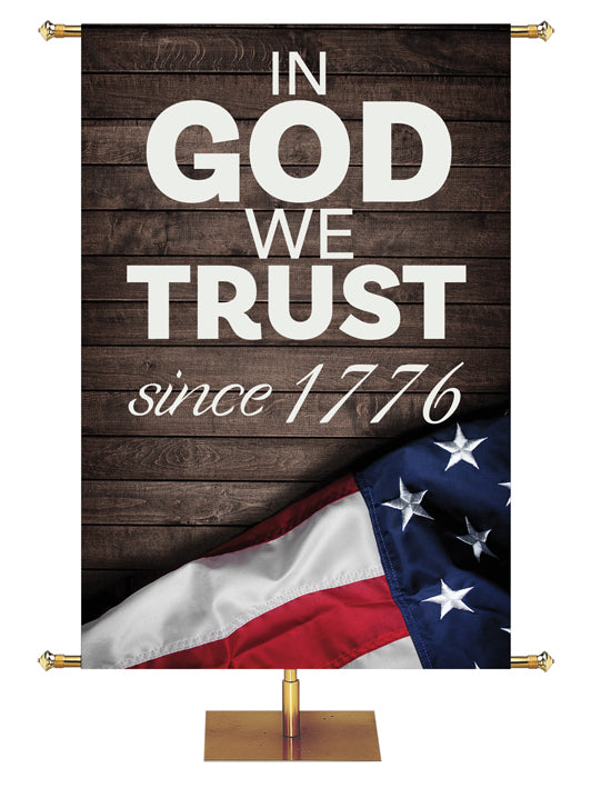 Patriotic Banner In God We Trust Since 1776 in white letters on dark barnwood background with flag with stars on the left