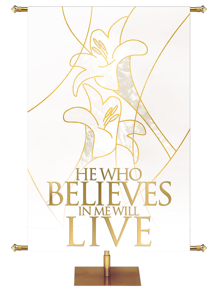 Easter Liturgy He Who Believes on White Banner with two Easter Lily Blooms right above left outlined in gold in wide banner format